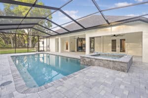 A screened-in patio for The Wyrick, featuring a swimming pool and a stone-tiled hot tub next to a house with a covered porch. Townsley Construction in Florida