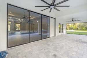 A covered patio with a stone paver floor, large sliding glass doors, and two ceiling fans, seen here in a Wyrick home plan. Townsley Construction in Florida