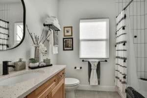 Bathroom in The Harper featuring a light-colored speckled vanity, a toilet, a window with a shade, and a bathtub with a white shower curtain accented by black geometric patterns. Townsley Construction in Florida