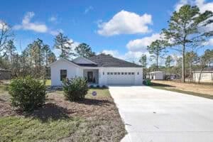 Single-story white Harper home with a two-car garage, a concrete driveway, three bedrooms, and two bathrooms. Townsley Construction in Florida