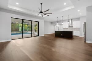 The Wyrick features an open-concept living area with wood floors, a kitchen with a dark island and white cabinetry, and sliding glass doors leading to a screened-in pool patio. Townsley Construction in Florida