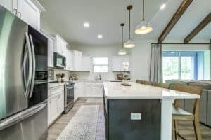 Modern kitchen in the Hamblin floor plan featuring white cabinets, stainless steel appliances, a large central island with bar seating, and three pendant lights hanging above. Townsley Construction in Florida