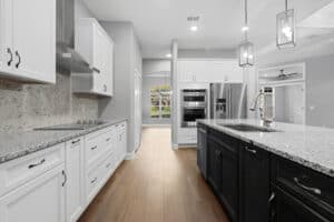 Modern kitchen in a 3 bedroom home with white perimeter cabinets, a dark island, stainless steel appliances, and light wood flooring. Townsley Construction in Florida