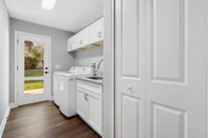 A laundry room with a washer and dryer, a sink, white cabinetry, and a glass-paneled door leading to an outdoor area in this Wyrick flex space. Townsley Construction in Florida