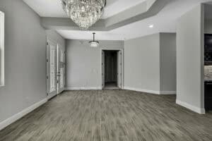 An empty flex room in The Purvis with light gray walls, wood-look tile flooring, two glass-paneled doors, and a large crystal chandelier. Townsley Construction in Florida
