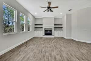 Empty flex room in The Purvis featuring wood-look tile flooring, a fireplace flanked by white cabinets, and built-in shelving. Townsley Construction in Florida