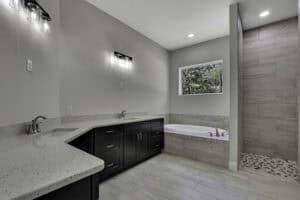 Bathroom in The Purvis featuring a dark wood double vanity, stone countertops, a deep soaking tub, and a walk-in shower with tiled walls and a pebble floor. Townsley Construction in Florida