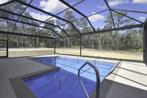 A rectangular swimming pool with a metal handrail, enclosed by a screen cage overlooking a wooded yard at The Purvis. Townsley Construction in Florida