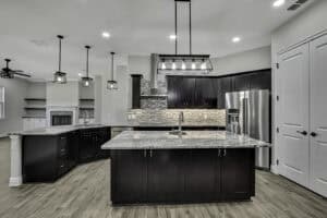 In this new construction home, a kitchen features dark wood cabinets, a large marble-topped island, stainless steel appliances, and pendant lighting. Townsley Construction in Florida