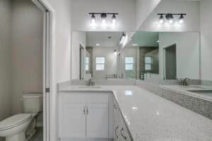 A 2 bath bathroom vanity with a speckled countertop and white cabinets, featuring a large mirror reflecting a toilet and shower area. Townsley Construction in Florida