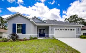 The Harper is a single-story grey house with dark blue shutters, a dark blue front door, and a white two-car garage. Townsley Construction in Florida