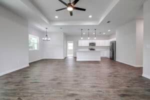 Open-concept living area in The Harper featuring wood-look flooring, a kitchen with white cabinets and an island, and a separate dining area with a chandelier. Townsley Construction in Florida