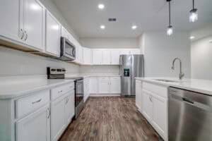 A modern kitchen in The Harper featuring white cabinets, stainless steel appliances, and a central island with a sink. Townsley Construction in Florida