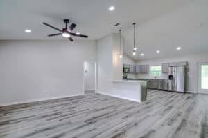 Open-concept living room and kitchen in this 4 bedroom Houston home, featuring light wood-look flooring, a black ceiling fan, and stainless steel appliances. Townsley Construction in Florida