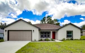 A single-story, four-bedroom Houston home with a light-colored exterior, a two-car garage, and a red front door. Townsley Construction in Florida