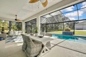 A screened-in patio for this Bennett floor plan home features a dining table with wicker chairs, a sofa seating area, and an outdoor swimming pool. Townsley Construction in Florida