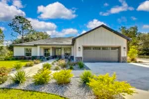 A single-story 3 bedroom house with white siding, a gray garage door, and a landscaped front yard with a concrete driveway. Townsley Construction in Florida