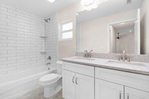A bathroom in a Houston home with a white double vanity, a toilet, and a bathtub with white subway tile walls. Townsley Construction in Florida