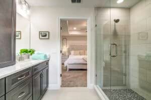 Bathroom featuring a dark vanity with a light countertop and a glass-enclosed shower, with a view into the bedroom of this Hamblin floor plan home. Townsley Construction in Florida