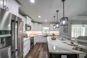 A modern kitchen in the Hamblin floor plan featuring white cabinets, stainless steel appliances, and a long island with a white marble countertop. Townsley Construction in Florida