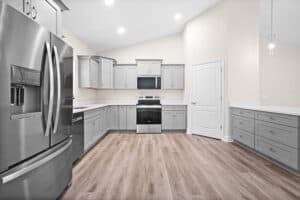A kitchen with gray cabinets, light countertops, and stainless steel appliances in a 4 bedroom house. Townsley Construction in Florida