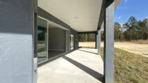 A covered concrete patio with sliding glass doors opening into a 3 bedroom home, overlooking a grassy field and trees. Townsley Construction in Florida