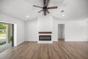 Living room in a new construction Hamblin home with wood-look tile flooring, a central fireplace with a wood mantel, and a ceiling fan. Townsley Construction in Florida