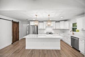 A kitchen with white cabinetry, a large central island, stainless steel appliances, and a wooden sliding barn door, designed for the Hamblin floor plan. Townsley Construction in Florida
