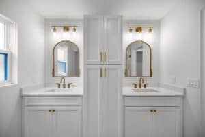Double vanity with white cabinets, white countertops, arched gold-framed mirrors, and gold wall-mounted light fixtures in a Hamblin 3 bedroom home. Townsley Construction in Florida