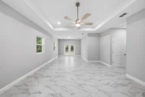 Empty flex space room with light gray walls, white marble-patterned tile flooring, and a ceiling fan in a tray ceiling, featuring a pair of glass-paned doors at the far end of the Bobak floor plan. Townsley Construction in Florida