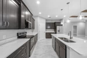 A modern kitchen in this Bobak floor plan features dark cabinetry, white marble-look countertops, stainless steel appliances, and a central island with a double sink. Townsley Construction in Florida