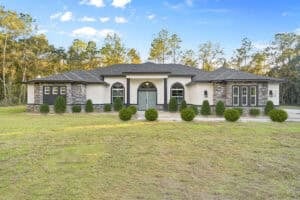 Single-story 3 bedroom home with a beige stucco and stone exterior, a dark grey roof, and a front lawn, with the number 1226 visible on the side. Townsley Construction in Florida