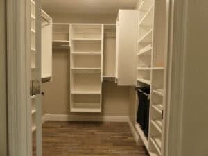 A walk-in closet in this 3-bedroom house featuring white shelving, hanging rods, and drawers on wood-look flooring. Townsley Construction in Florida