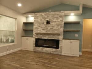 A stone-tiled fireplace with an electric insert, mantel, and flanking white cabinets with open wooden shelving in the Hamblin flex space. Townsley Construction in Florida