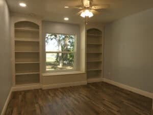 A flex space with light blue walls, wood-look flooring, built-in bookshelves flanking a center window with a bench seat, and a ceiling fan. Townsley Construction in Florida