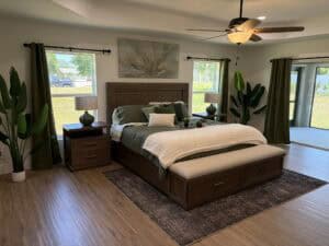 A king-sized bed sits in this 3 bedroom house, framed by dark wood furniture, green curtains, and potted plants on either side. Townsley Construction in Florida