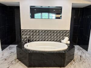 An oval soaking tub in The Wyrick is set into a black marble surround with a patterned tile backsplash and a wall-mounted rectangular mirror. Townsley Construction in Florida