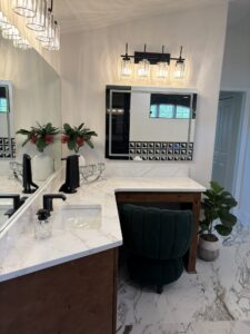 Bathroom vanity in The Wyrick with white marble countertops, dual mirrors, dark wood cabinetry, and a dark green velvet stool, creating a sophisticated flex space. Townsley Construction in Florida