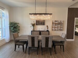 Dining room in the Wyrick floor plan featuring a rectangular wood table, six upholstered chairs, and a long crystal chandelier hanging above. Townsley Construction in Florida