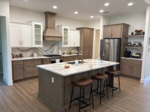 A kitchen in The Wyrick with a central island and three bar stools, featuring two-tone cabinetry, a marble-patterned countertop and backsplash, and a stainless steel refrigerator. Townsley Construction in Florida