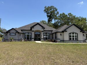 Single-story Wyrick suburban house with light gray stucco walls, dark trim, and a large front lawn under a clear blue sky. Townsley Construction in Florida