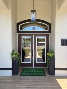 The entrance to Townsley Construction at The Wyrick features double glass doors, a green branded floor mat, and two tall planters flanking the doorway. Townsley Construction in Florida