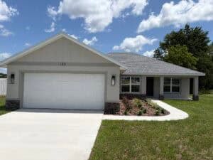 The Bailey is a 3 bedroom, 2 bath house featuring a single-story beige exterior, a white two-car garage, and the address number 133 above the garage door. Townsley Construction in Florida