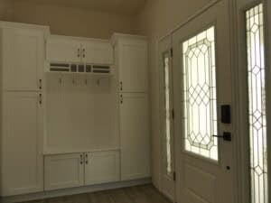 White built-in entryway storage with cabinets and coat hooks next to a glass-paneled door in The Harper, a 3 bedroom home. Townsley Construction in Florida