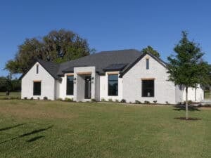 Single-story 4 bedroom white brick house with a dark roof and black window frames set in a grassy yard. Townsley Construction in Florida