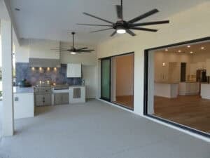 An outdoor kitchen with a grill and blue hexagonal tile backsplash on the patio of this 4 bedroom house, featuring large sliding glass doors that open into an indoor kitchen. Townsley Construction in Florida