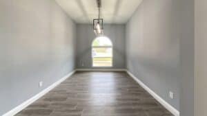 Empty room with gray walls, wood-look tile flooring, and a central arched window under a hanging lantern light fixture, perfect as a flex space in this home. Townsley Construction in Florida
