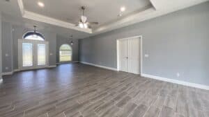 A spacious, empty flex space in this 3-bedroom home with grey walls, wood-look tile flooring, white double doors, and two arched windows. Townsley Construction in Florida